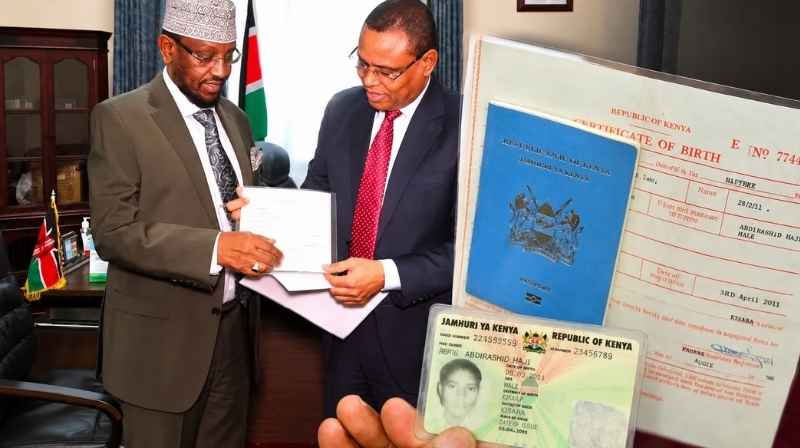 Somalia Deputy Prime Minister Jibril Abdirashid Haji hands over documents while a Kenyan passport, birth certificate and national ID are displayed following the passport surrender.